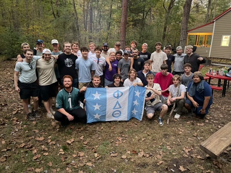 Brothers gathered outdoors at a retreat, holding the Phi Delta Theta flag